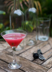 Red cocktail with ice in glass with stem on wooden surface