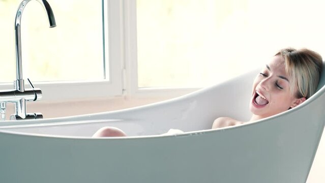 Portrait of young beautiful sexy woman having fun while lying in bathtub full of foam at home. Charming smiling model relaxing in luxury bath interior. Female enjoying beauty and skincare day