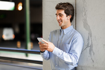 Smiling young guy employee using smartphone and earphones