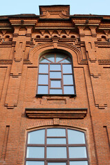 Two storeys of red brick historical building with windows on its front part standing in front of camera in old area of modern city