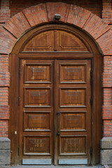 Fototapeta na wymiar Closed wooden door on front part of red brick historical institution which represents place of interest for tourists of modern city
