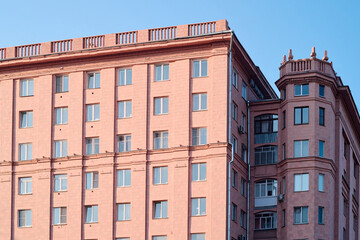 Fototapeta premium Part of classic real estate building or block of flats of pink color standing against blue sky in the center of modern city