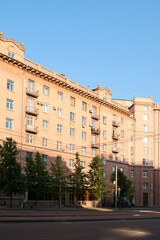 Obraz premium Part of municipal building or block of flats surrounded by green trees standing along road in downtown of modern city
