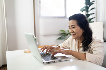 Fototapeta na wymiar Middle age Asian woman Work from home. senior woman smiling Beautiful mature asian woman on laptop with technology concept