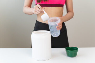 Young sporty woman pouring protein powder into a cup to make replacement food meal after workout
