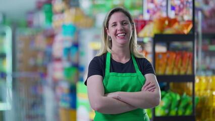 Portrait of a joyful woman employee of grocery store laughing and smiling with arms crossed standing inside supermarket aisle looking at camera. job occupation concept