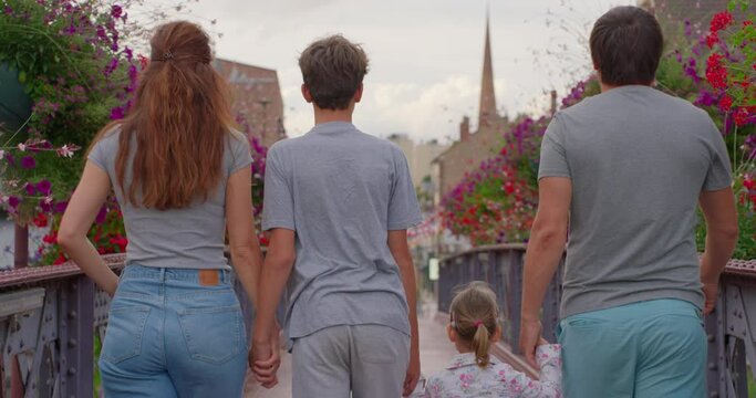 A large family of four are walking through a colorful park. A family with children of three and thirteen years old spend time together on the street of a big city in Europe