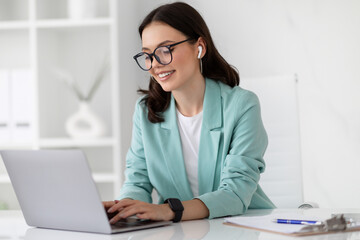 Positive young caucasian business woman in suit, glasses with computer work, enjoys professional...