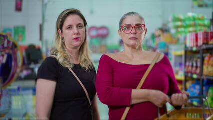 Stern Faced Middle-Aged Female Customers Holding Baskets Inside Grocery Store, Serious Women Posing at Supermarket
