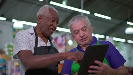 Teamwork at Grocery Store, Older Manager Guiding Employee through Tablet Device Operations