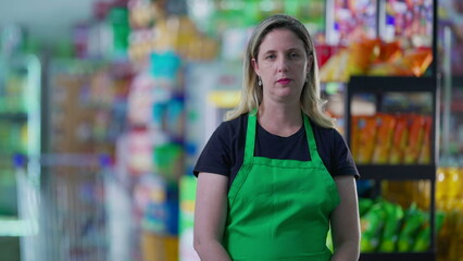 Serious female employee of Supermarket wearing green apron, middle-aged staff of Grocery Store with stern worried expression during difficult times, job occupation