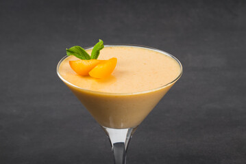 Apricot cream jelly dessert, Panna Cotta, decorated with fresh apricot slices, in a martini glass. Dark gray background. Close up
