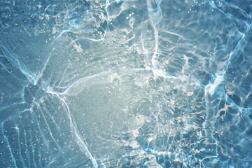 Blue water with ripples on the surface. Defocus blurred transparent blue colored clear calm water surface texture with splashes and bubbles. Water waves with shining pattern texture background.