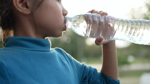 A little girl drinking water from plastic bottle.