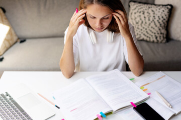 Student young brunette woman doing homework, thinking about exercise in her educational student's book, sitting at the desk and studying.