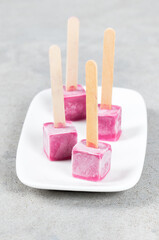 Black currant ice creams in the shape of small cubes on a wooden stick. On a plate.