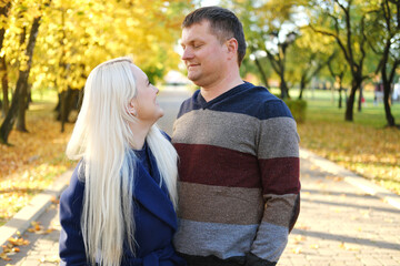 Married couple posing in autumn park. Man and woman look at each other in love