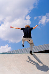 A young guy skater does a stunt on the edge of a skatepool against a backdrop of sky and clouds at...