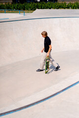 Young guy skateboarder with long hair skateboarding and doing tricks in the skate pool at the city...