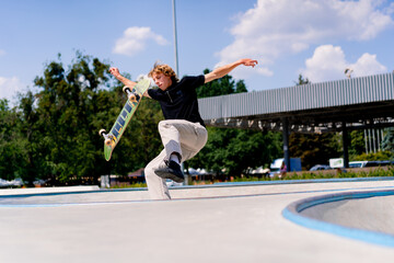 A young boy skater falls while performing a stunt on the edge of a skatepool against the sky and...