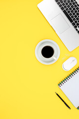 Work space layout with notepad, laptop and coffee cup on a yellow background.