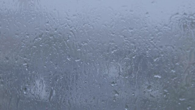 water droplet from rain fall condense during storm on window glass with cold and blue environment feeling with cloudy sky in rainy season