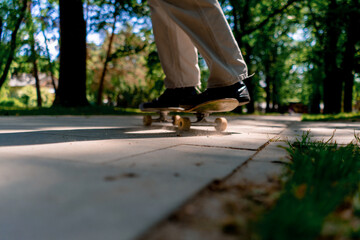 young guy skater rides a skateboard on the path of the city park against the background of trees and sky close-up