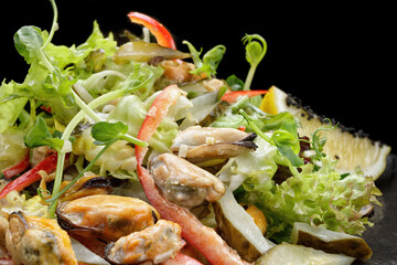Salad with mussels, on a black plate