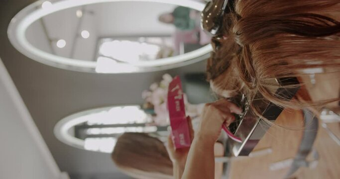 Professional hairdresser adding hair extensions for brunette girl in a beauty salon, vertical video, trucking, selective focus