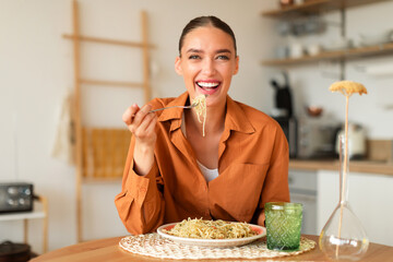Happy young european lady eating homemade Italian pasta, enjoying tasty lunch, sitting in kitchen...