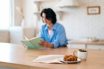 Croissants and cup with coffee against reading woman on background