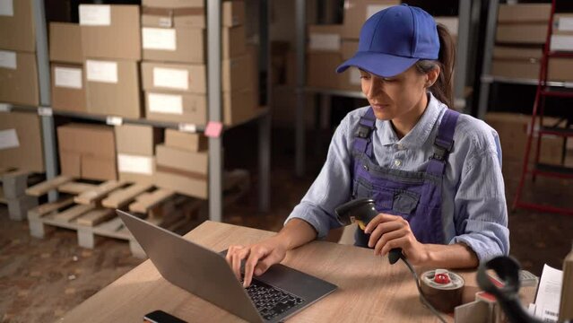 Female worker scanning barcode of shipment at her desk using laptop. Woman working in a drop-shipping office, preparing parcels for delivery.