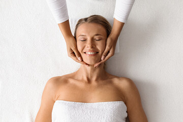 Therapist making lifting facial massage for beautiful middle aged lady, top view