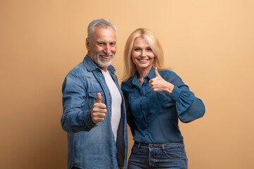 Positive elderly couple showing thumb up on beige background