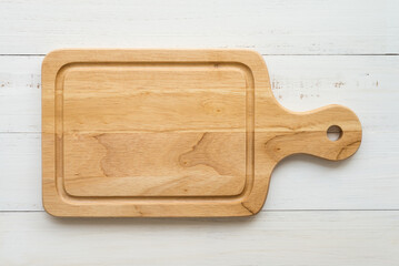 Top view of unused brand new brown handmade wooden cutting board on white wooden table background.