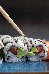 Vertical closeup shot of a pair of chopsticks over a plate of gourmet sushi rolls