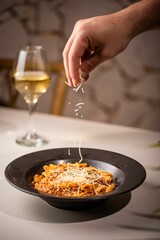 Person sprinkling cheese on a bowl of delicious pasta with meat and sauce