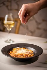 Person sprinkling cheese on a bowl of delicious pasta with meat and sauce