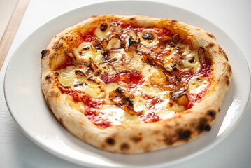 Delicious freshly-baked pizza with ham and melted cheese on a plate on the table