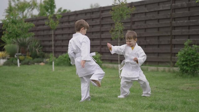 Little cheerful funny kids playing karate in white suit in the garden