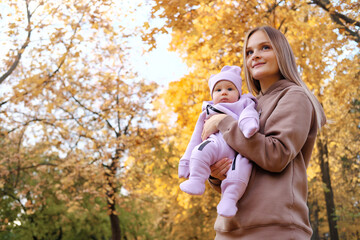 Young mother walking with her newborn daughter in the autumn park. Mother holds the girl in her arms, smiles and looks away