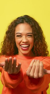 Flirty young woman beckons with hands 'come here', yellow studio background