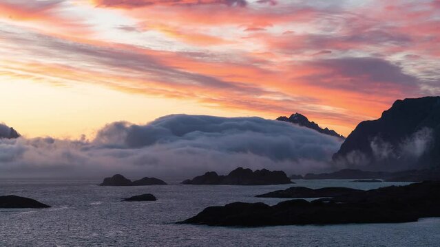Timelapse of the low clouds and fog surrounding the big cliffs and the sea during the pink sunset