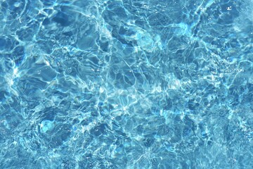 Blue water with ripples on the surface. Defocus blurred transparent blue colored clear calm water surface texture with splashes and bubbles. Water waves with shining pattern texture background.