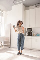 Full-length photo of cheerful female using wireless headphones and dancing on the kitchen while...