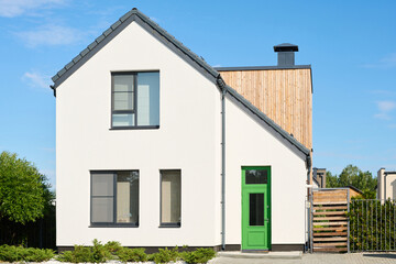 Facade of white two storey cottage surrounded by small green plants and bushes growing along pathway in rural environment