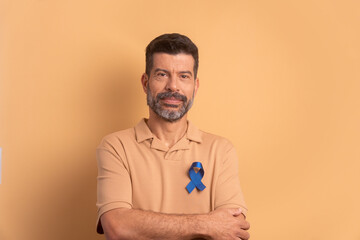 confident caucasian man showing blue ribbon in beige background. prostate cancer, awareness concept.