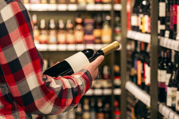 A male customer holding a bottle of red wine, close up.