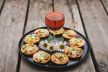 a small snack, pizzas piccolo on black plate with a glass of wine, on a wood table