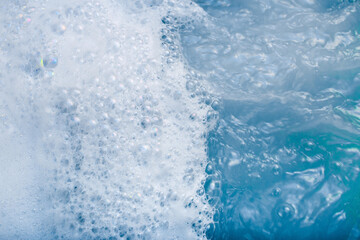 white cosmetic foam texture on blue water background. Bath foam. Cleanser, shampoo bubbles, wash -...